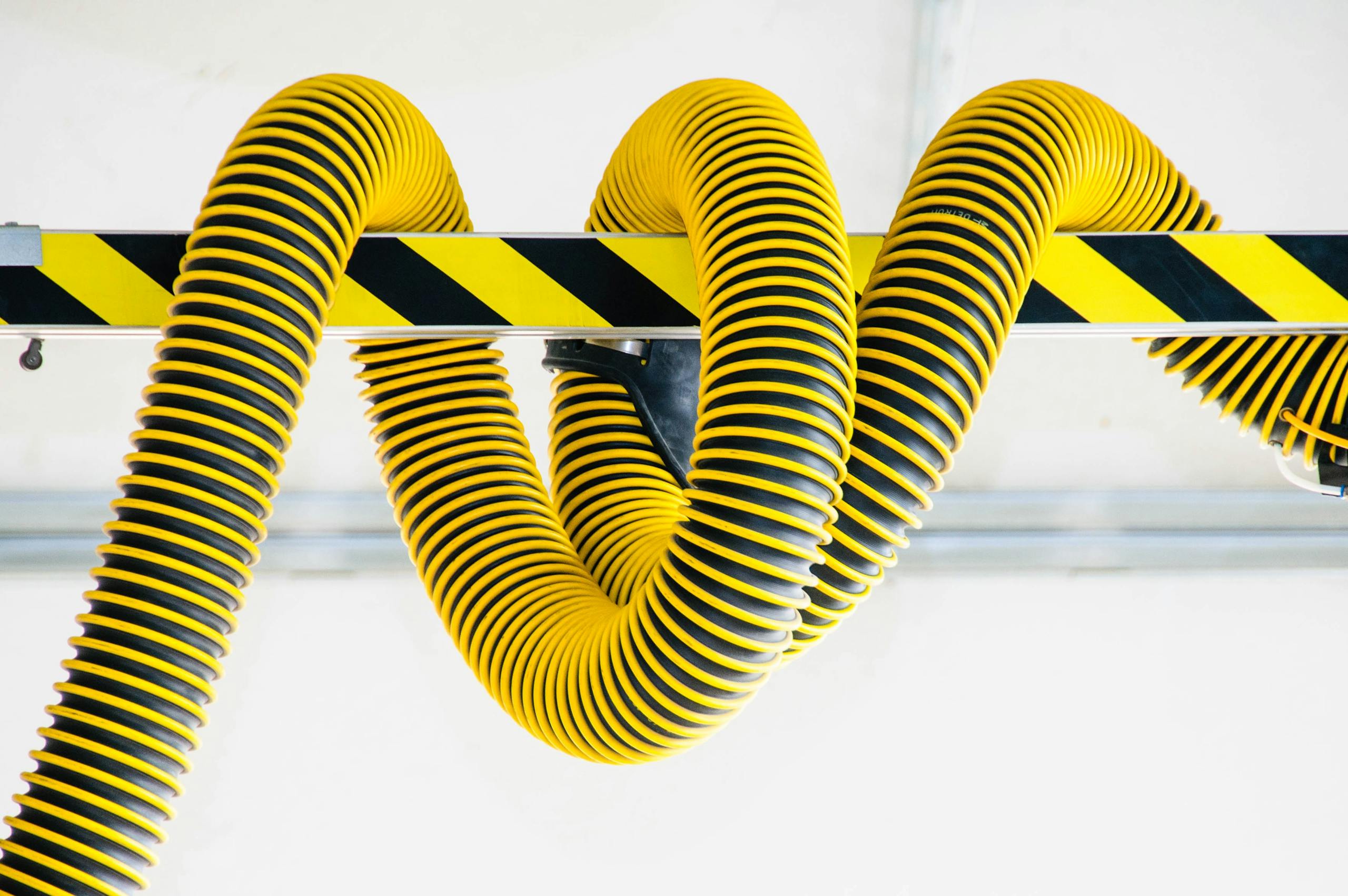 Close-up of yellow industrial hoses coiled around a safety-striped metal beam, showcasing modern industrial design.
